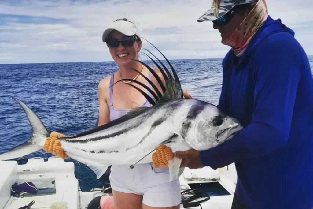 Angler and captain holding a trophy roosterfish with its dorsal crest fully extended on a charter boat off Playa Potrero, Costa Rica