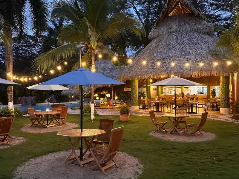 Garden dining area with string lights and thatched-roof palapa at a Playa Potrero resort at dusk