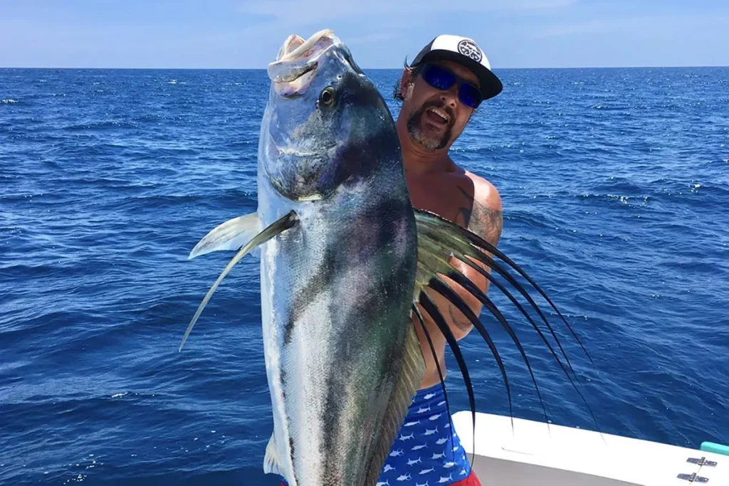 Angler holding a large roosterfish with its dorsal comb fully flared, aboard a charter on the Pacific off Guanacaste