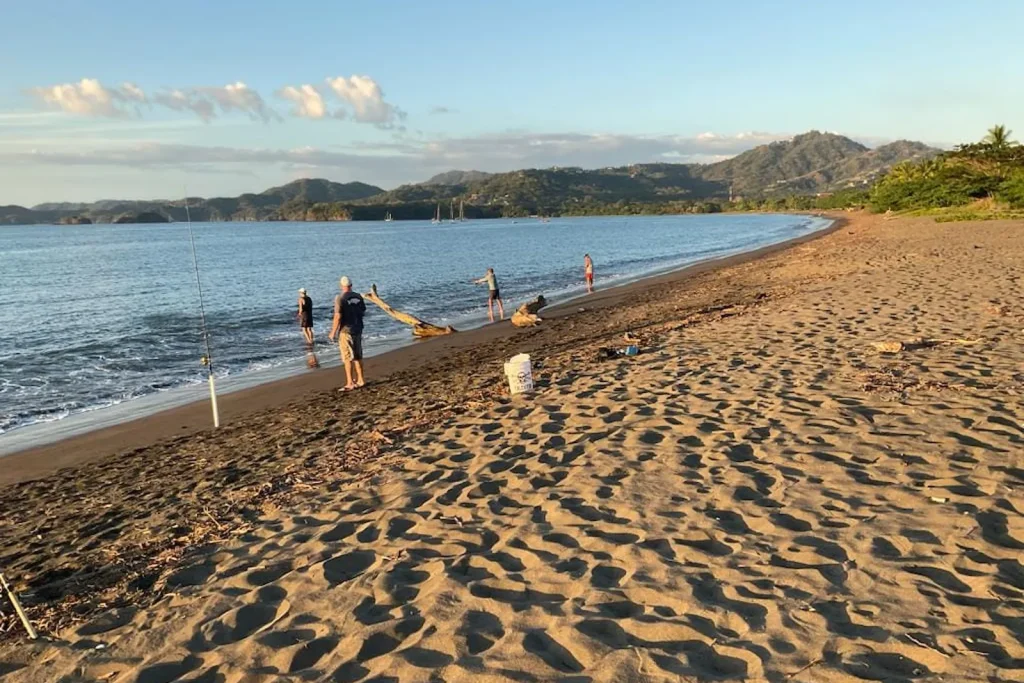 A group surf fishing on the sand at golden hour with the Potrero bay and headlands behind them