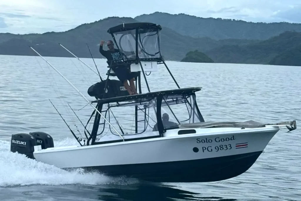 The Solo Good sportfishing boat underway off Playa Potrero, Costa Rica, twin Suzuki engines and tower, captain waving