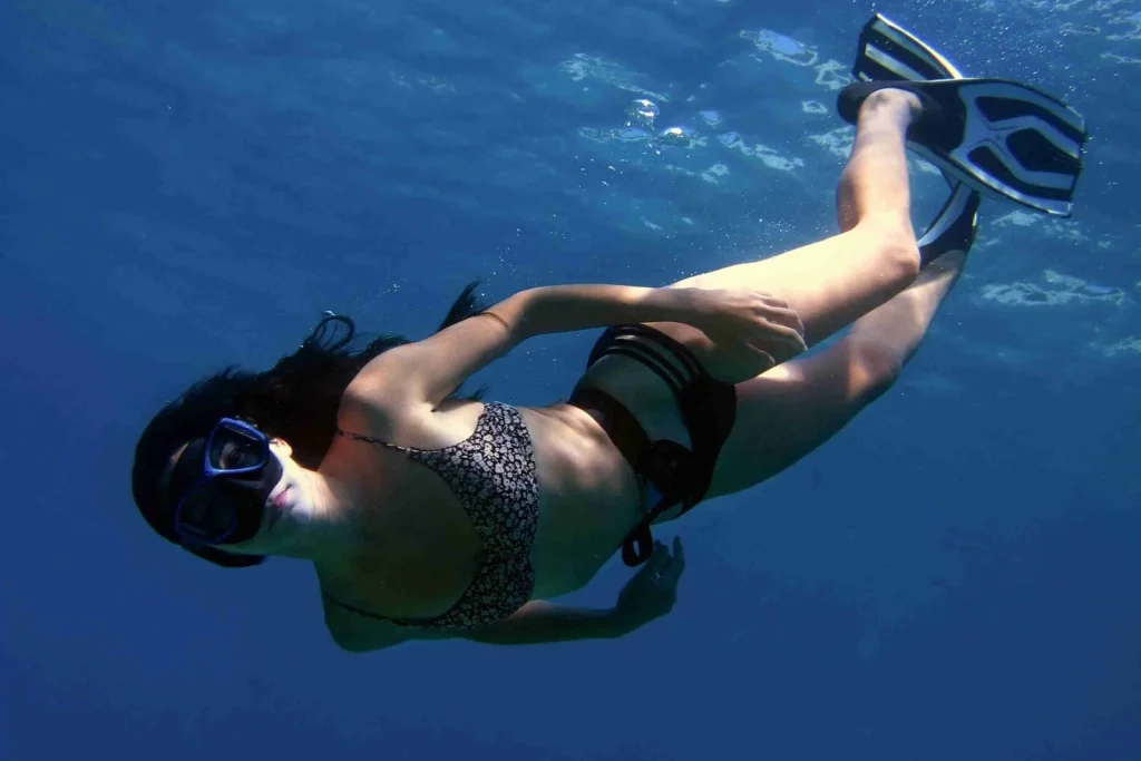 A woman freediving underwater in a swimsuit and fins through the clear blue Pacific water off Playa Potrero, Costa Rica