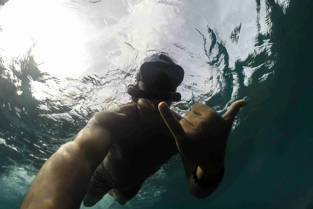 A snorkeler at the surface flashing a shaka sign with sunlight breaking through the water above, snorkeling in Guanacaste, Costa Rica